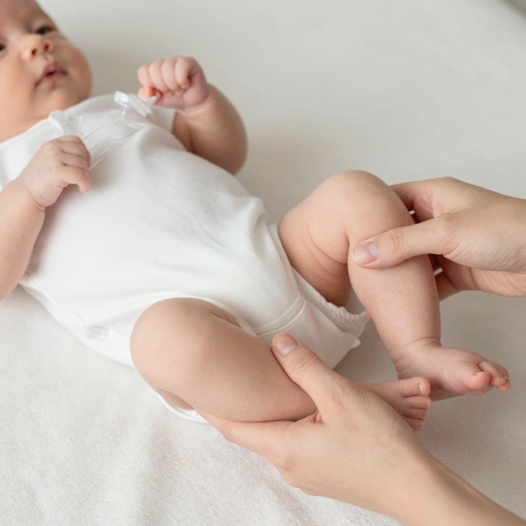 Parent holds newborn baby's legs performing bicycle movements on soft blanket.