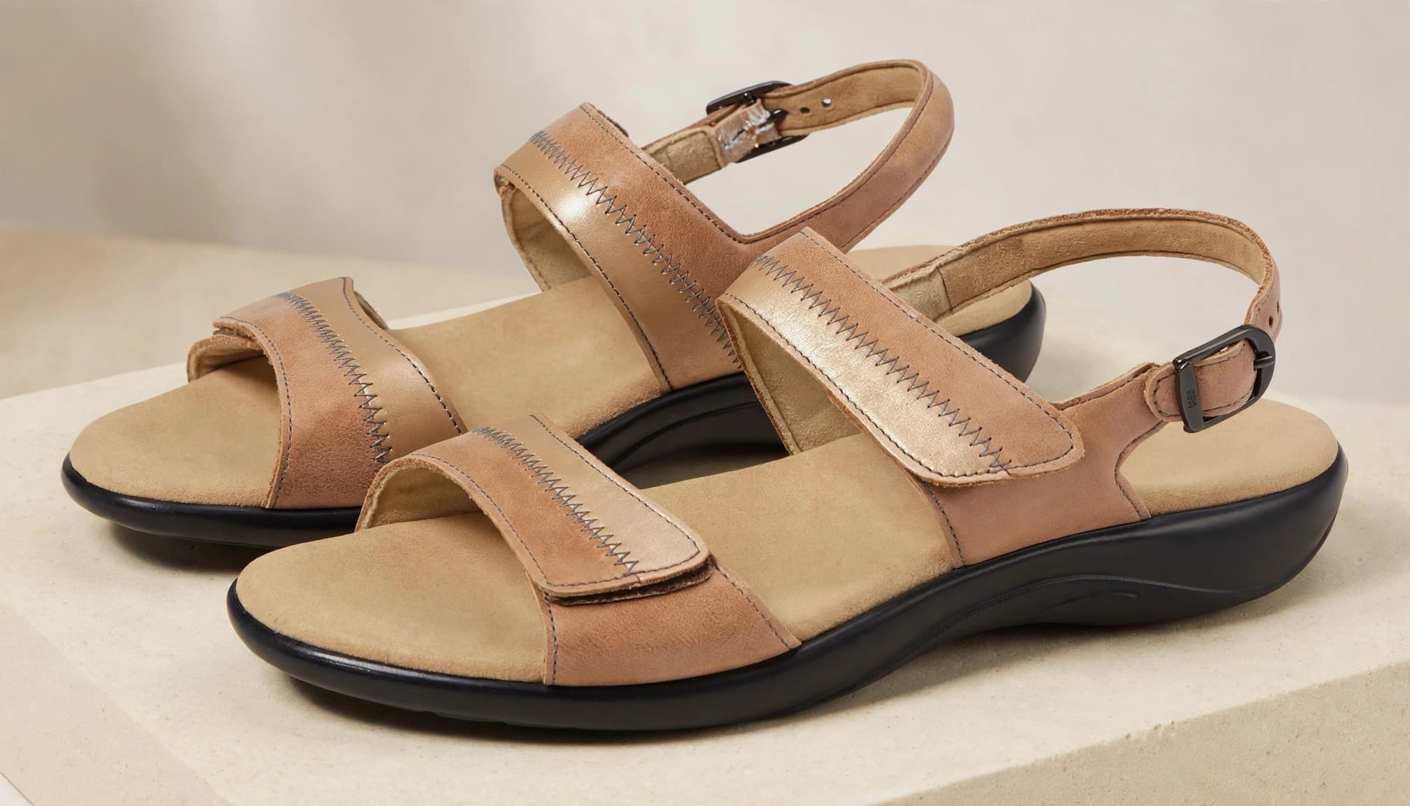 Two leather sandals with buckled straps and contoured footbeds on a pale plinth.