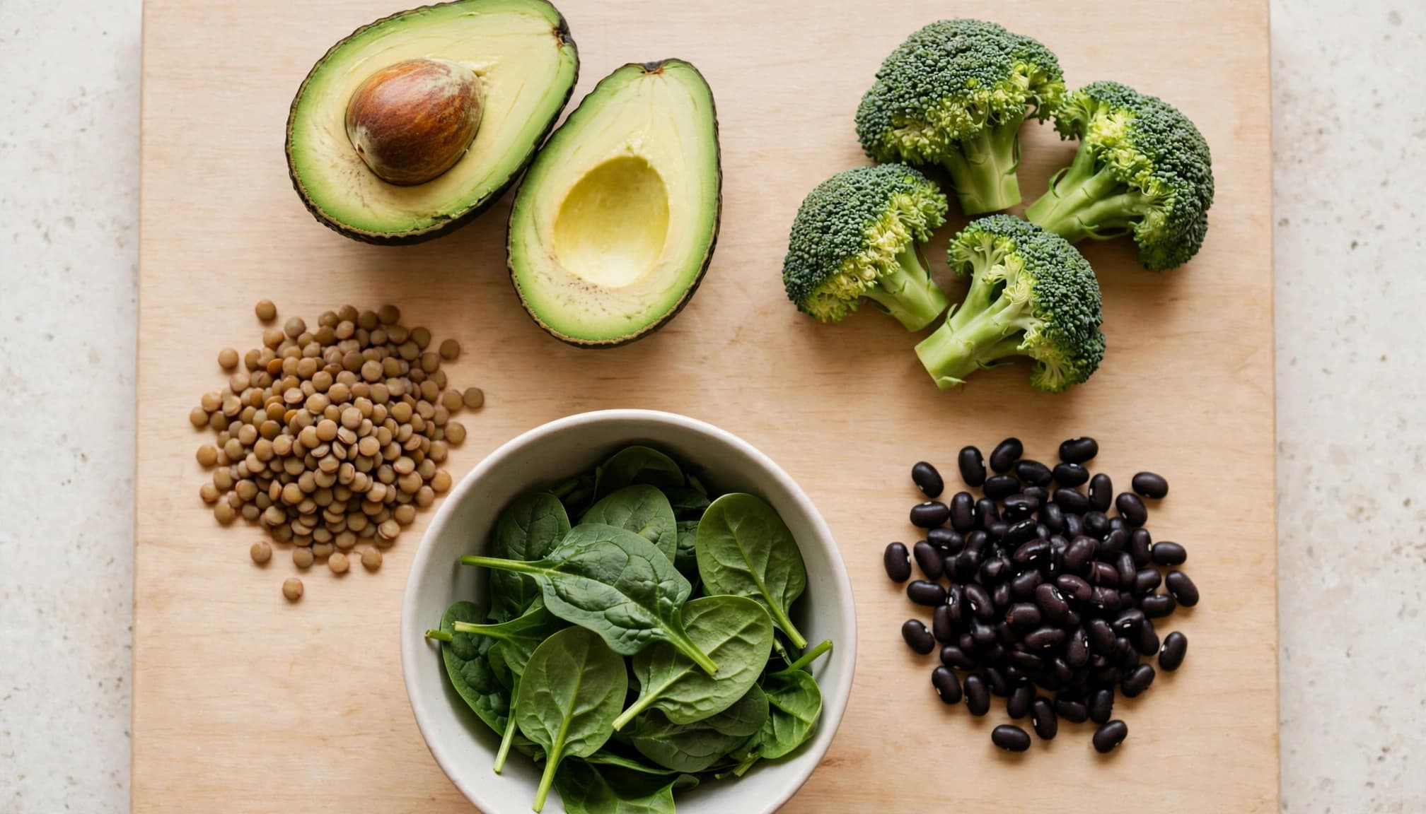 Avocado, lentils, spinach, broccoli, and black beans arranged around a ceramic bowl.