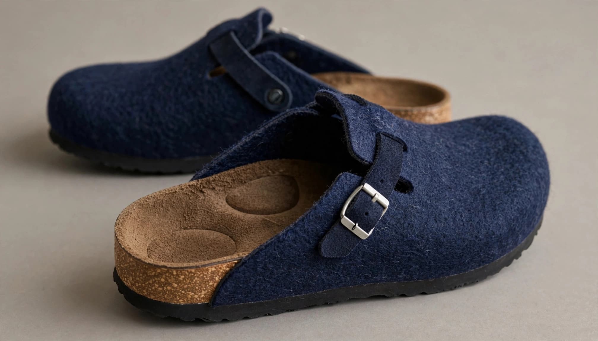 Two navy wool clogs, with the front shoe tilted to show its contoured sole.