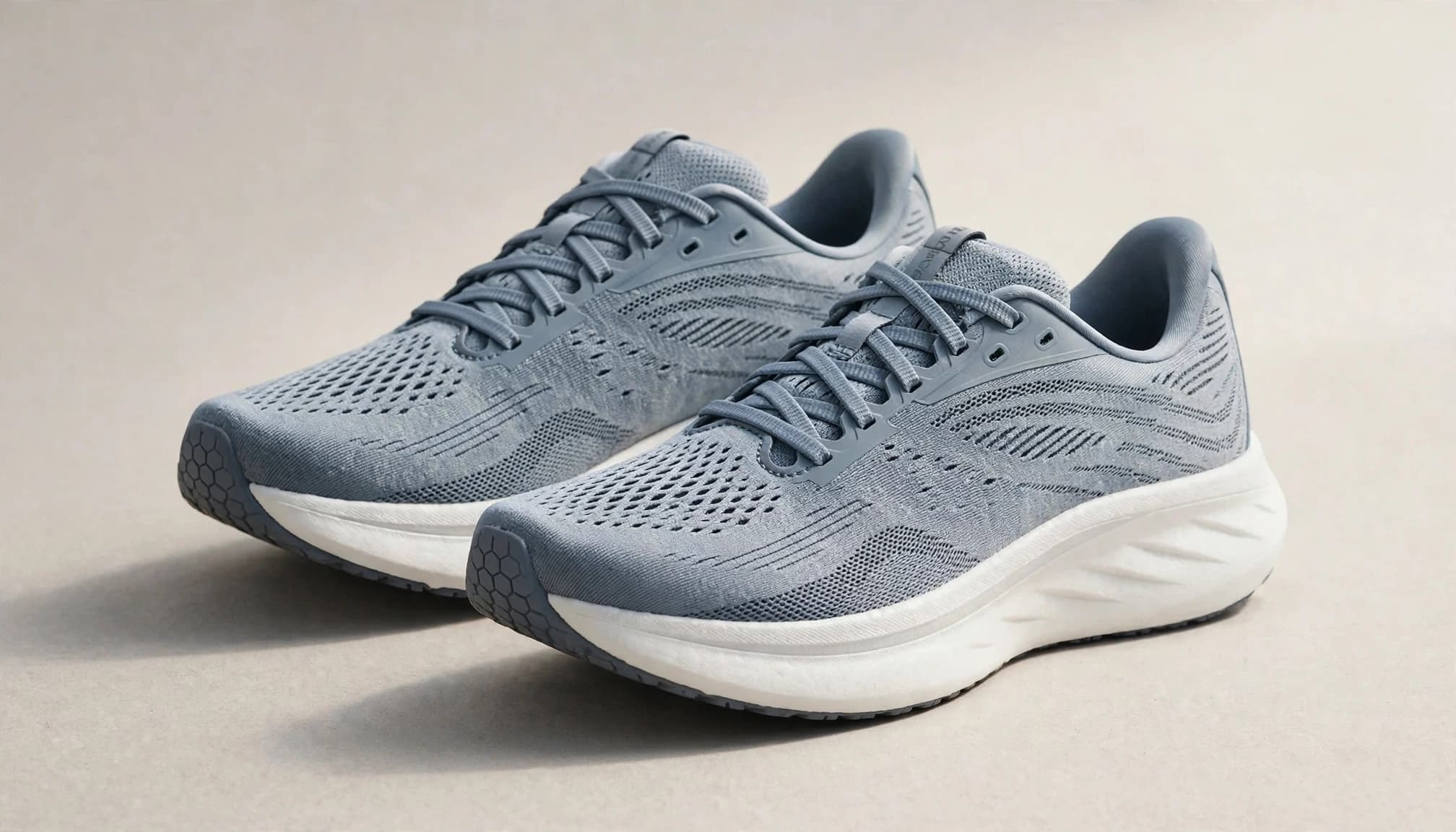 A pair of neutral running shoes on a warm gray studio surface.