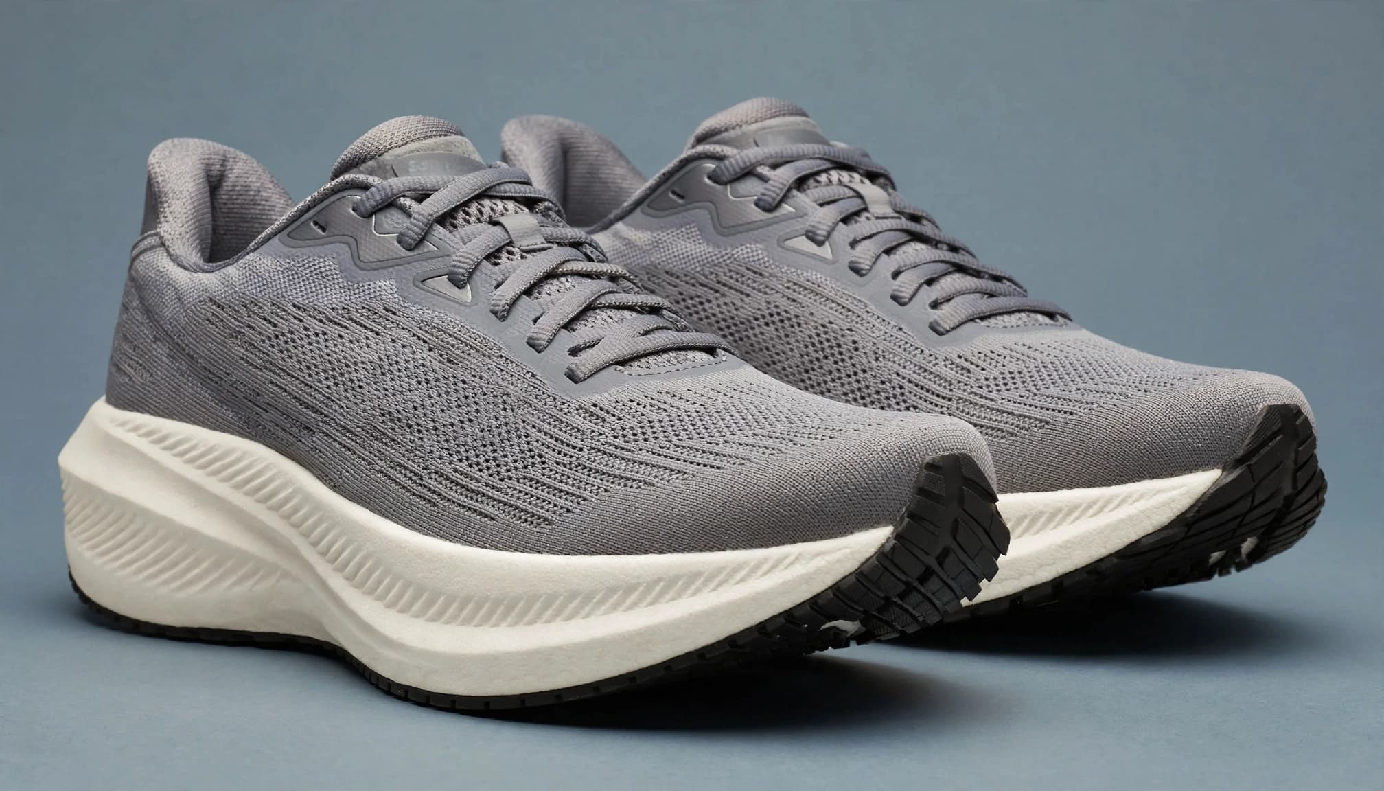 A pair of cushioned running shoes on a blue-gray studio surface.
