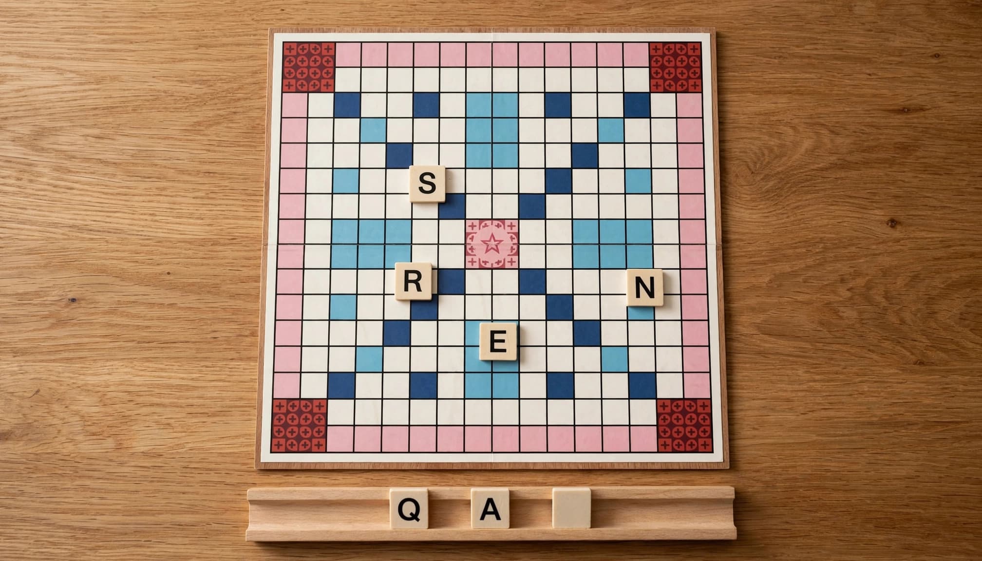 Een woordspelbord met gespeelde tegels en een rekje met een Q, een A en een blanco joktegel.