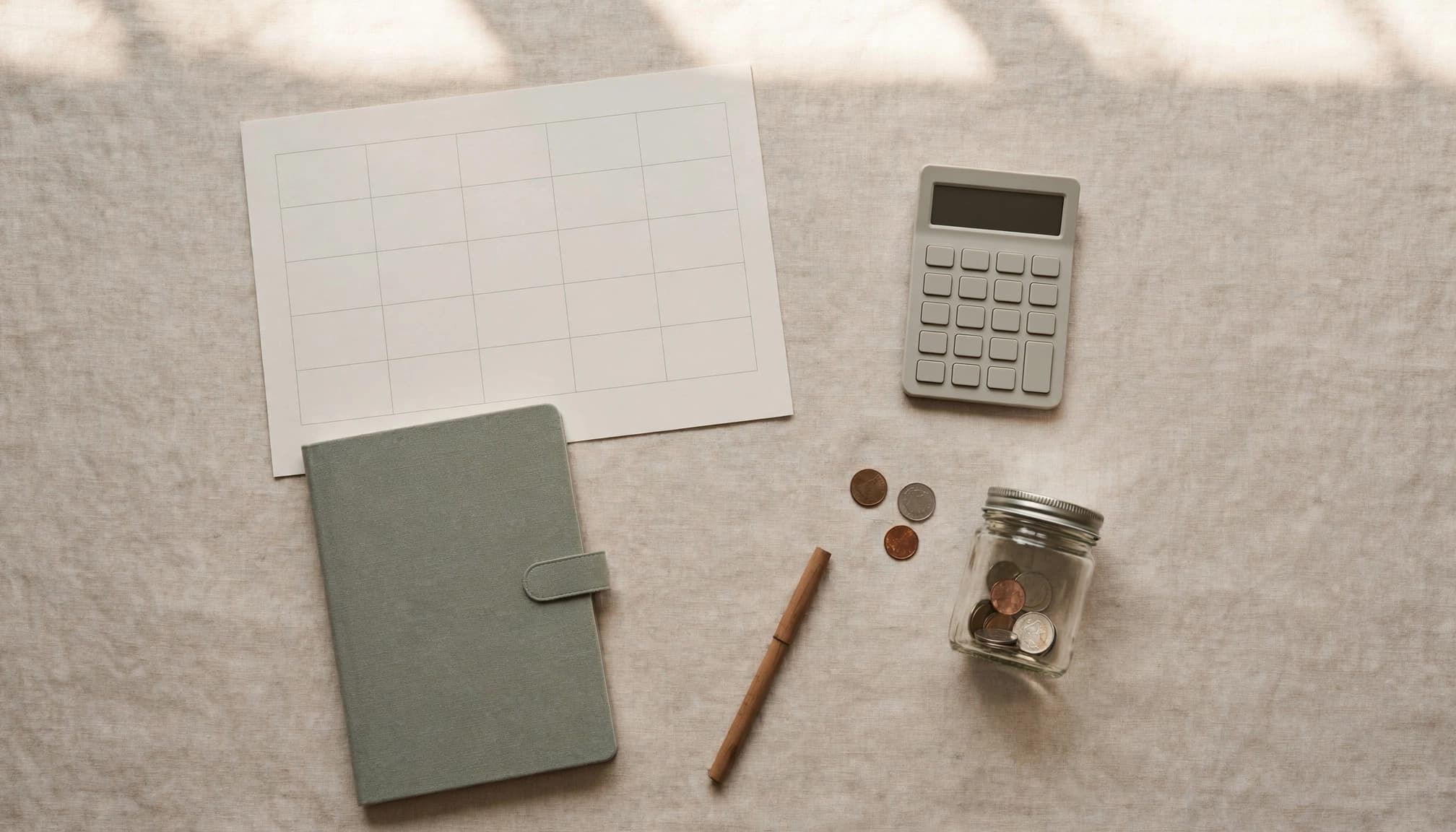 A blank calendar, notebook, calculator, pen, and coin jar arranged on a desk.