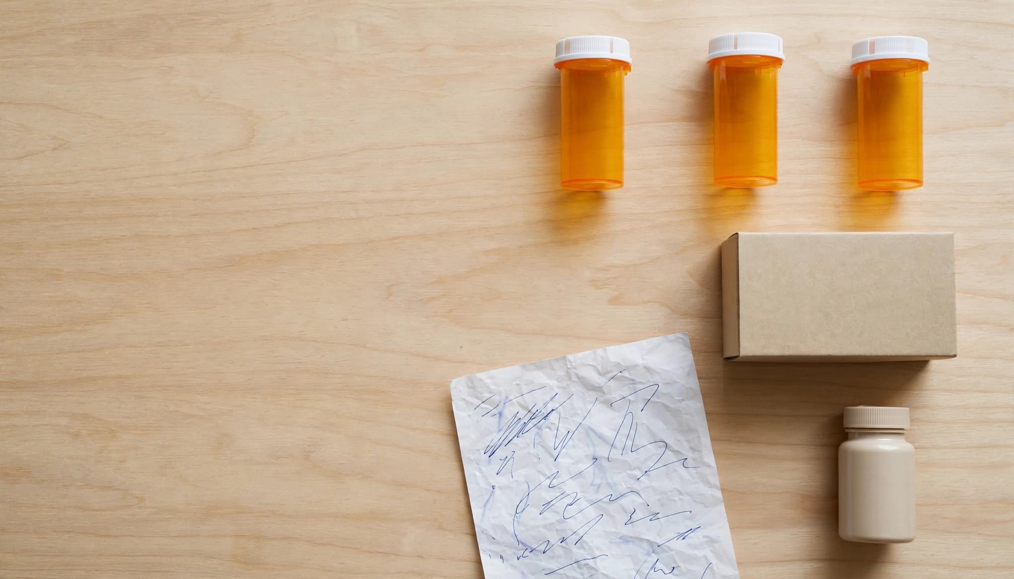 Medicine bottles and a handwritten list arranged on a sunlit dining table.