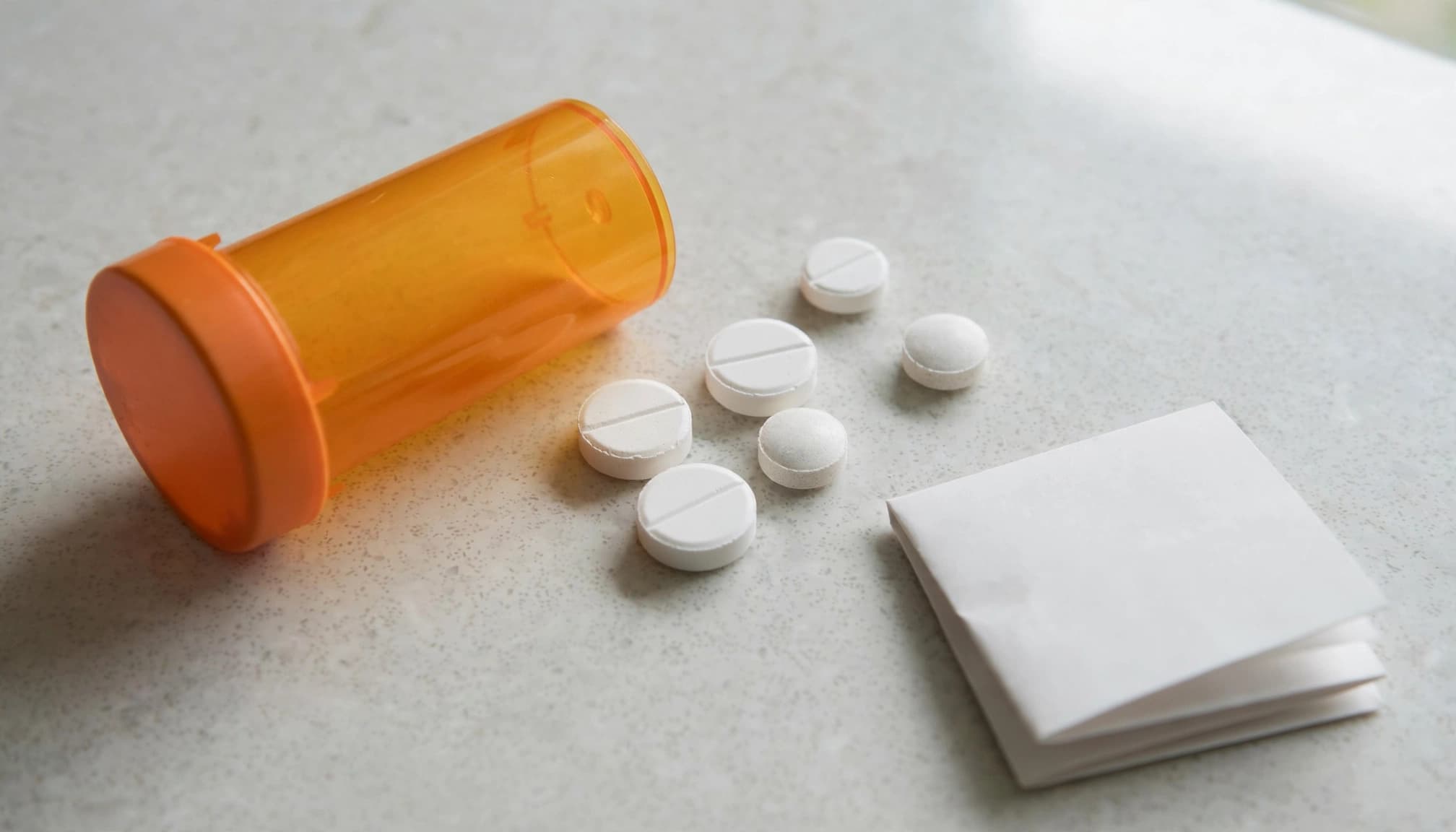 An orange prescription bottle, loose tablets, and a folded medication list on a counter.