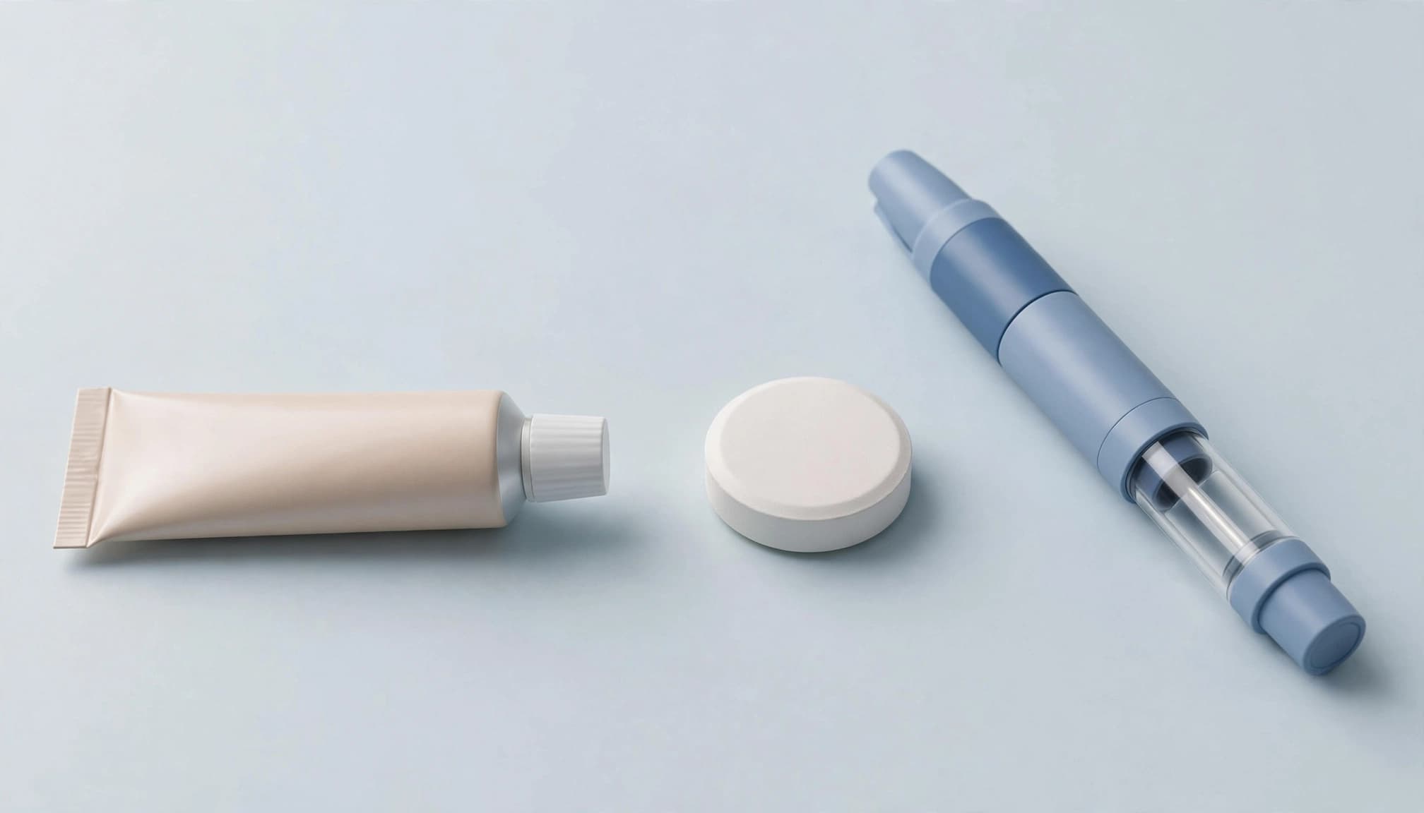 A tube of cream, a white tablet, and an injection pen arranged horizontally on a neutral surface.