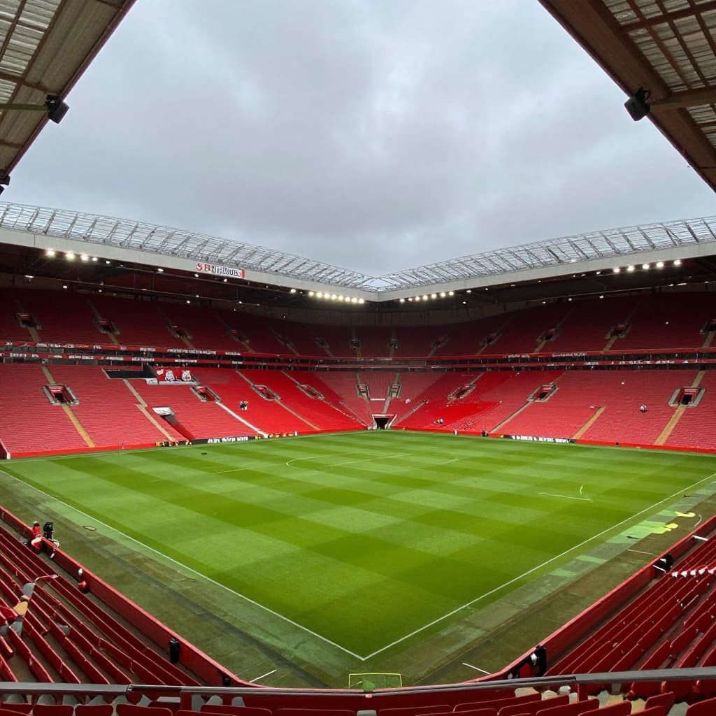 A low-angle view from the pitch looking up at the towering, vacant red stands of Anfield stadium.