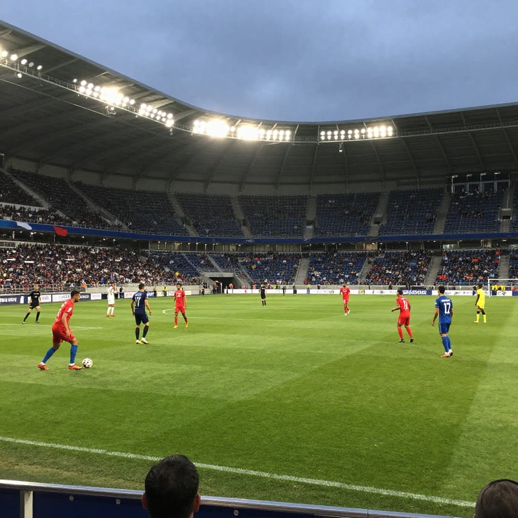 Two football teams compete for possession on a grass pitch under bright stadium lights.
