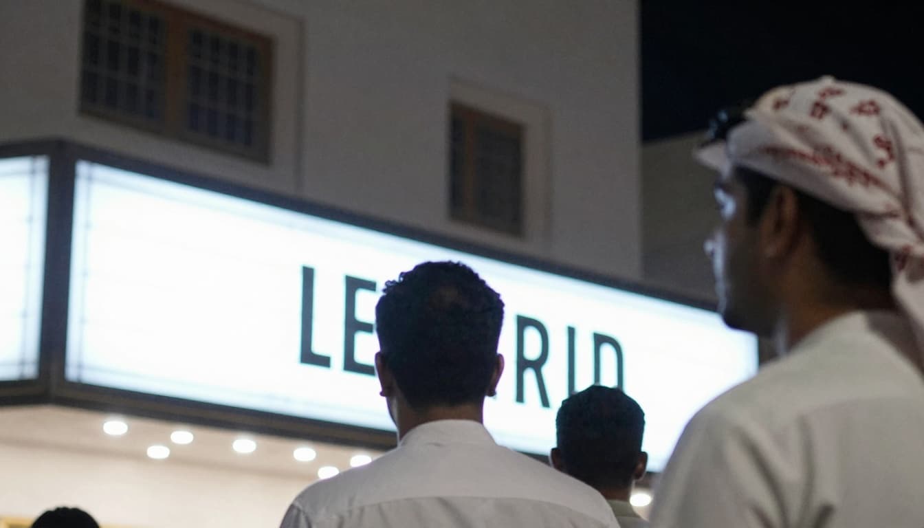 Theater marquee at night with bright lights and a crowd in silhouette waiting in line