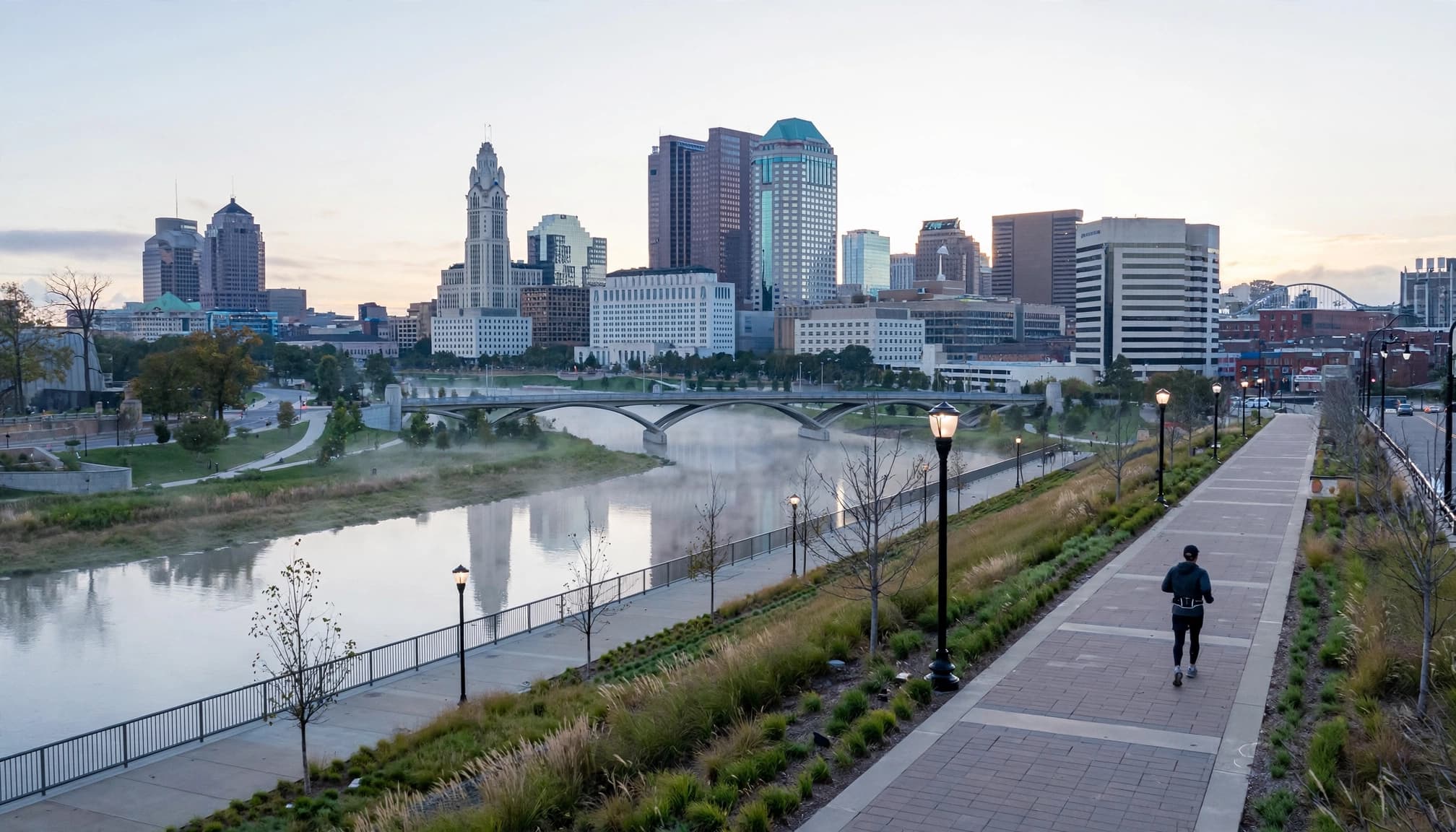 One runner walks beside the Scioto River with Columbus buildings and bridges in the distance.