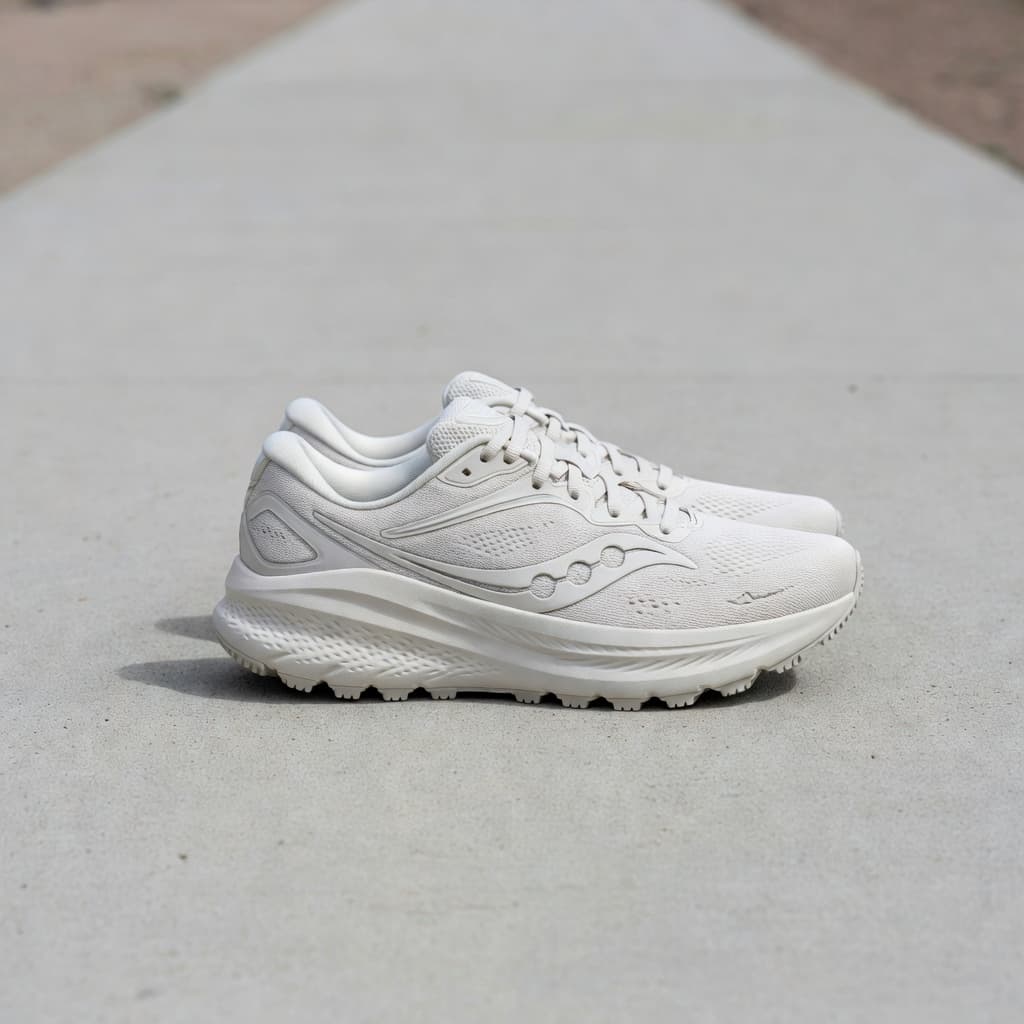 A pair of neutral running shoes sits on a smooth grey concrete surface under bright daylight. The side view highlights the thick cushioning, stable wide base, and supportive geometry of the footwear.