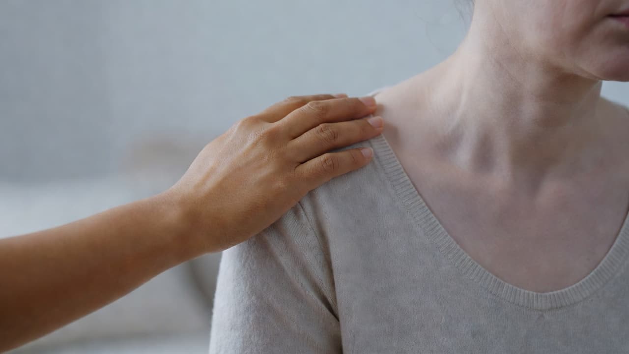 Kopertekort simptome agter bleek vel en moegheid Natuurlike Medisyne A comforting hand rests gently on a person's shoulder against a soft, muted background. The warm lighting emphasizes a calm atmosphere intended to highlight physical signs of fatigue and wellness.