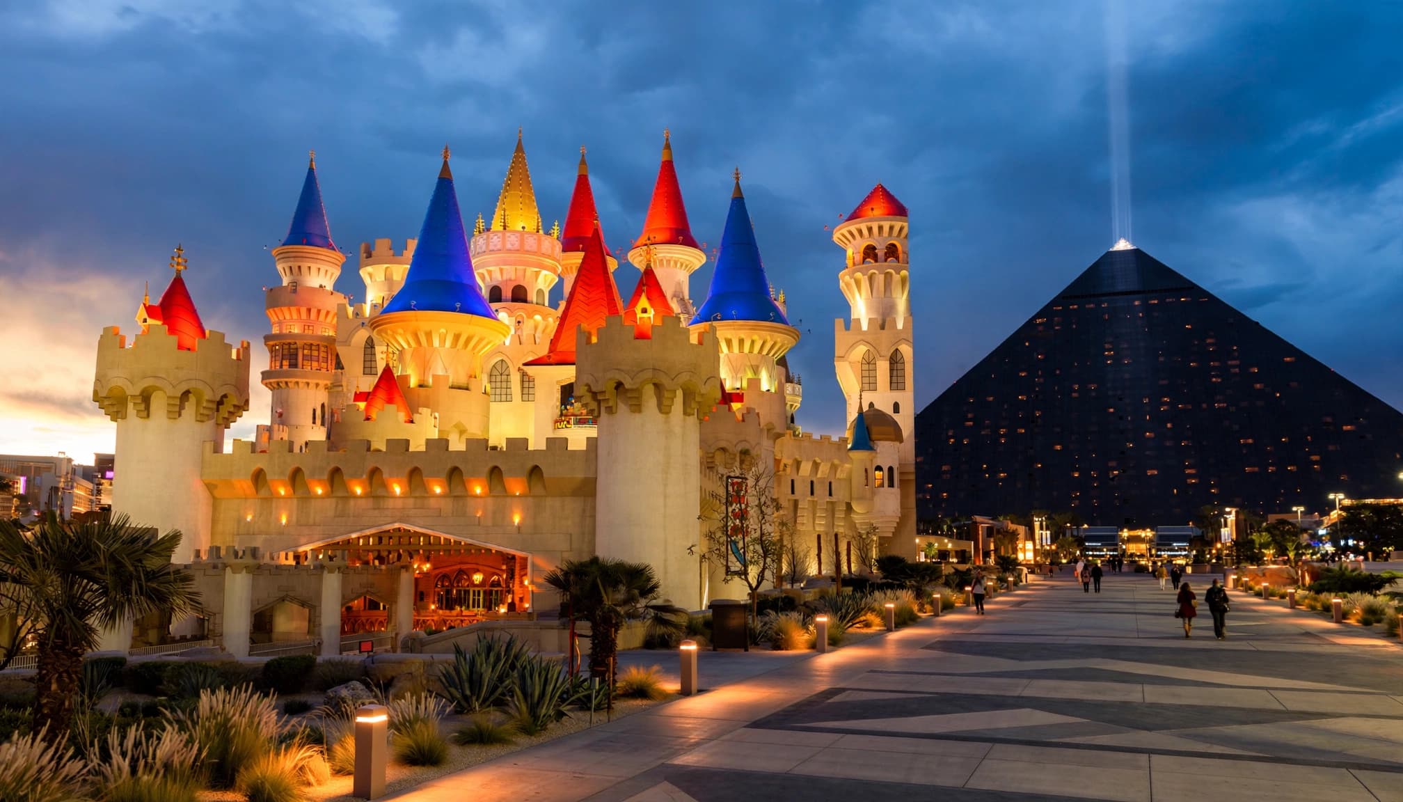 A medieval-style castle resort and a black glass pyramid at dusk.