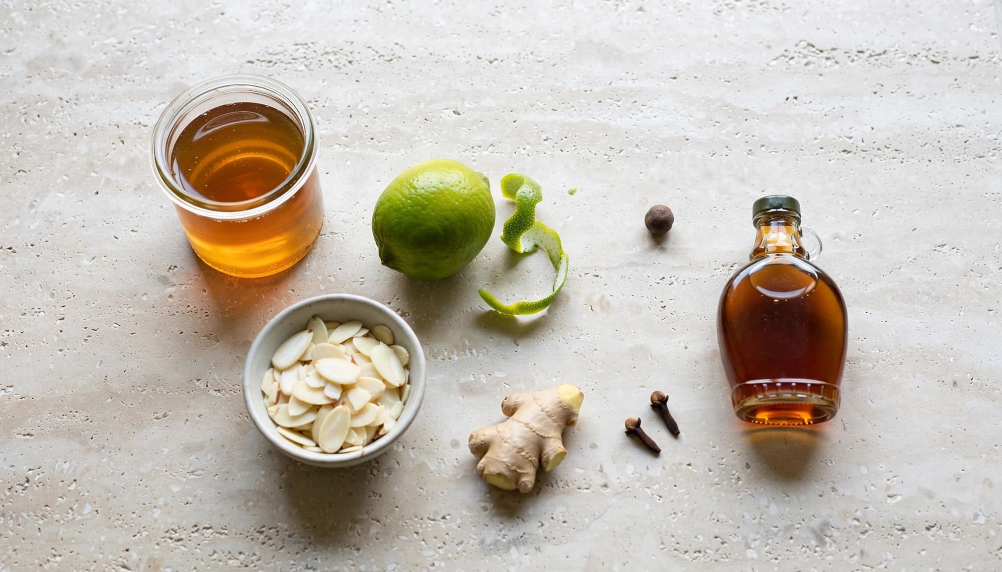 Un pot de sirop ambré avec du sirop d'érable, du citron vert, des amandes, du gingembre, des clous de girofle et du quatre-épices.