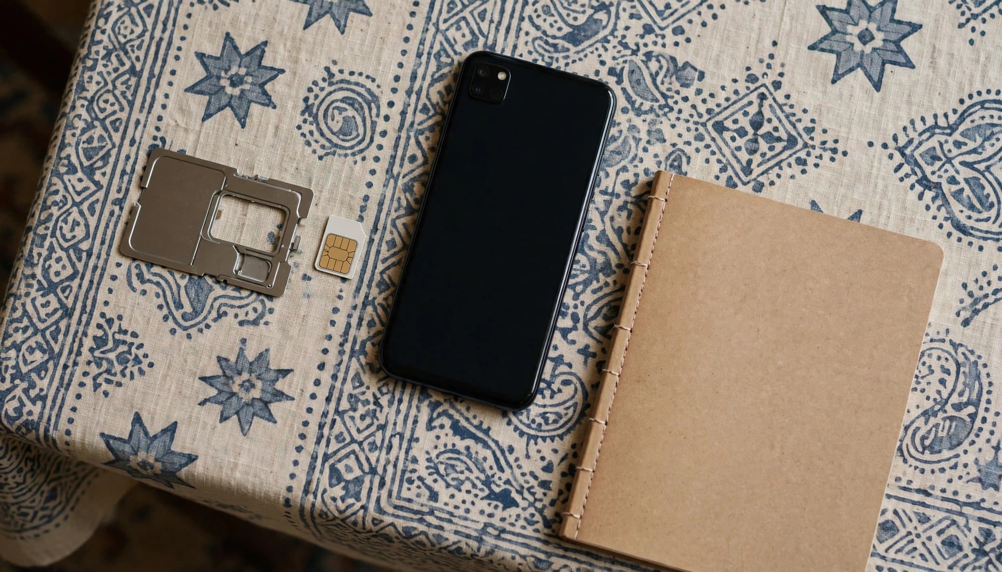 A SIM card and tray beside a dark smartphone and notebook on a small entry table.
