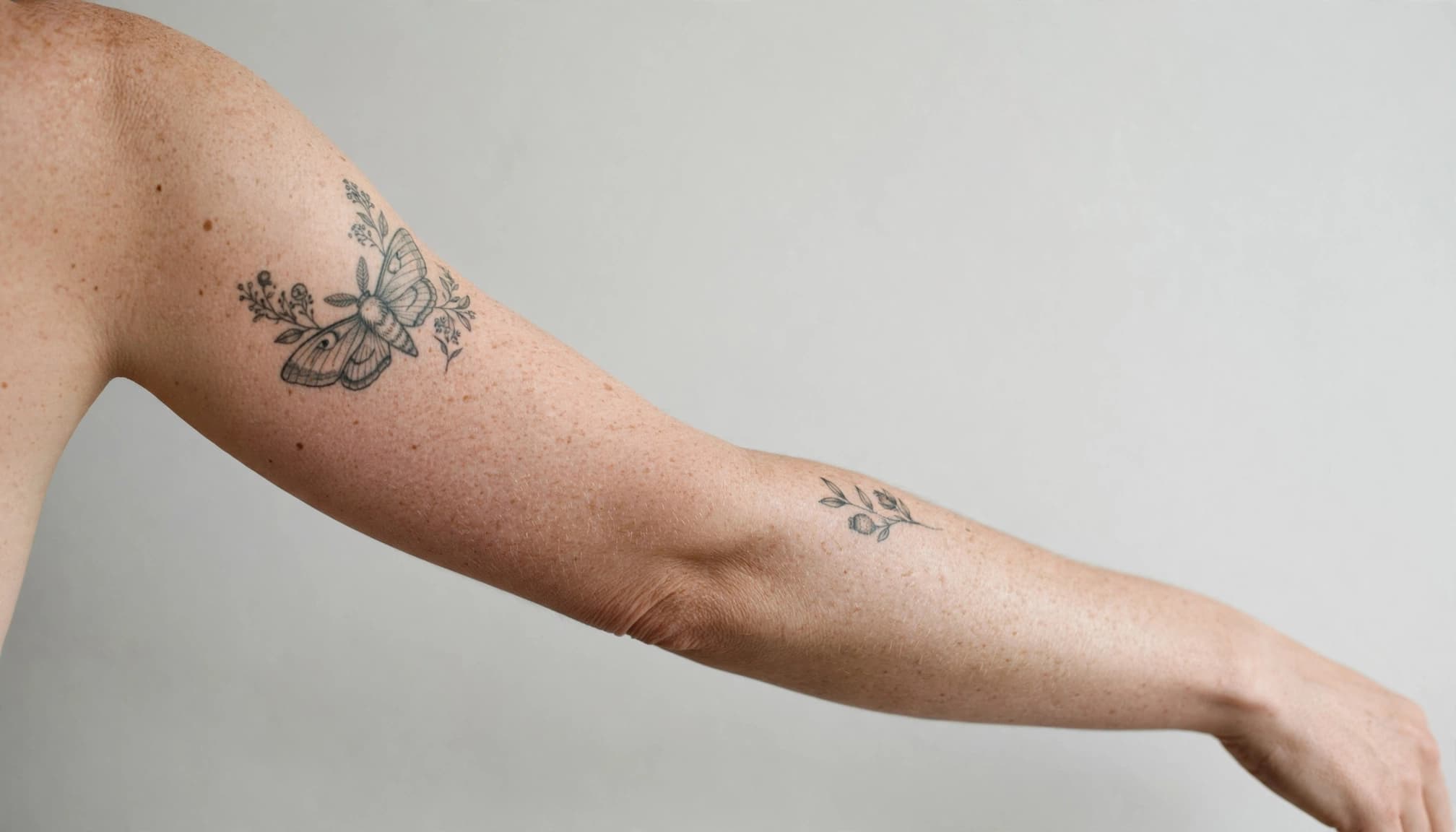 A cropped arm with a small botanical tattoo and a larger illustrative tattoo.