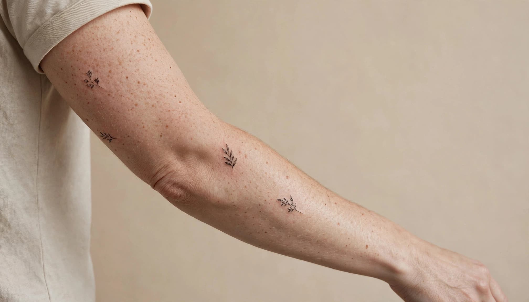 A small black botanical tattoo on one naturally posed arm against a warm studio background.