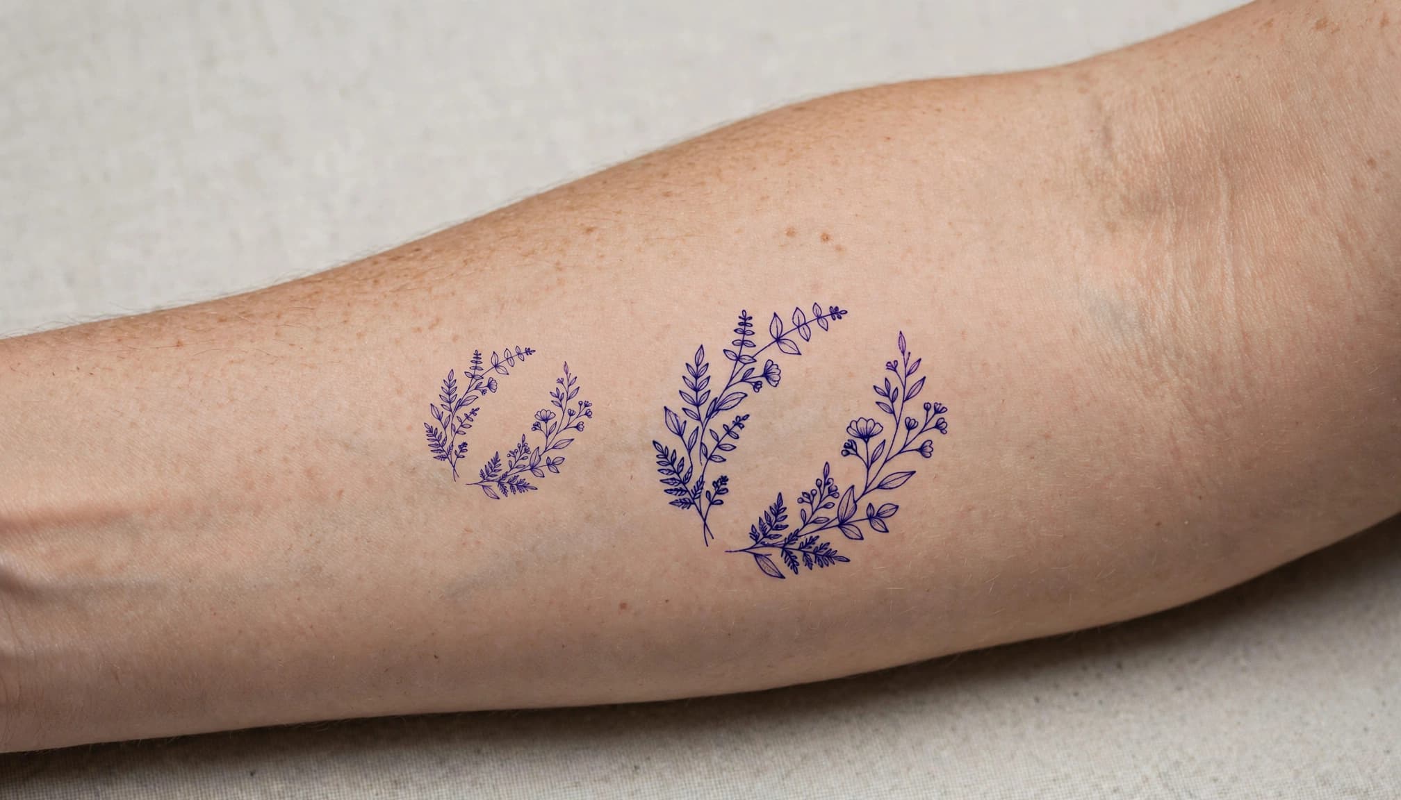 Two botanical tattoo stencils in different sizes sit side by side on one forearm.