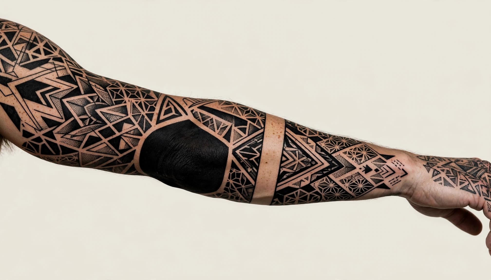 An arm with a geometric black tattoo sleeve and a bare band across the forearm.