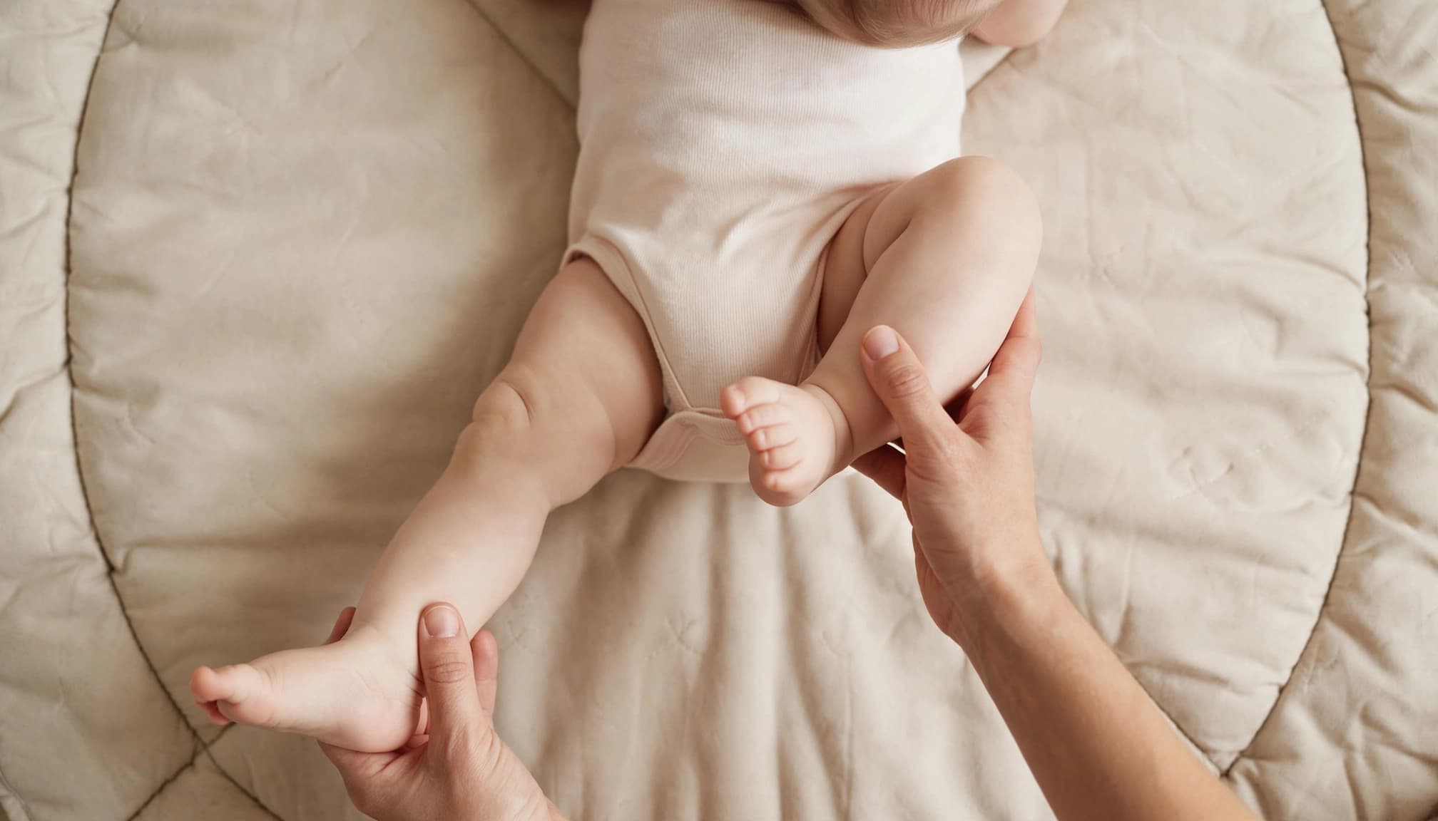 Caregiver gently moves a baby's legs in a bicycle motion on a soft mat.