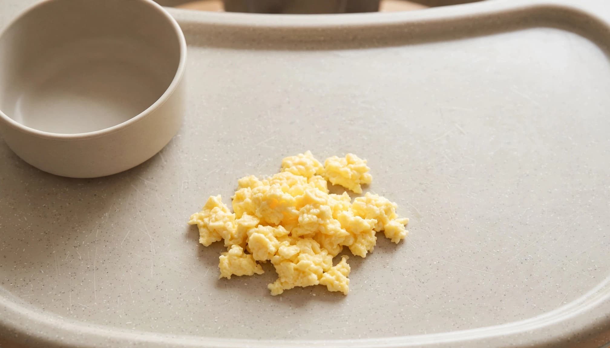 Soft scrambled egg on a clean high-chair tray beside a plain bowl.