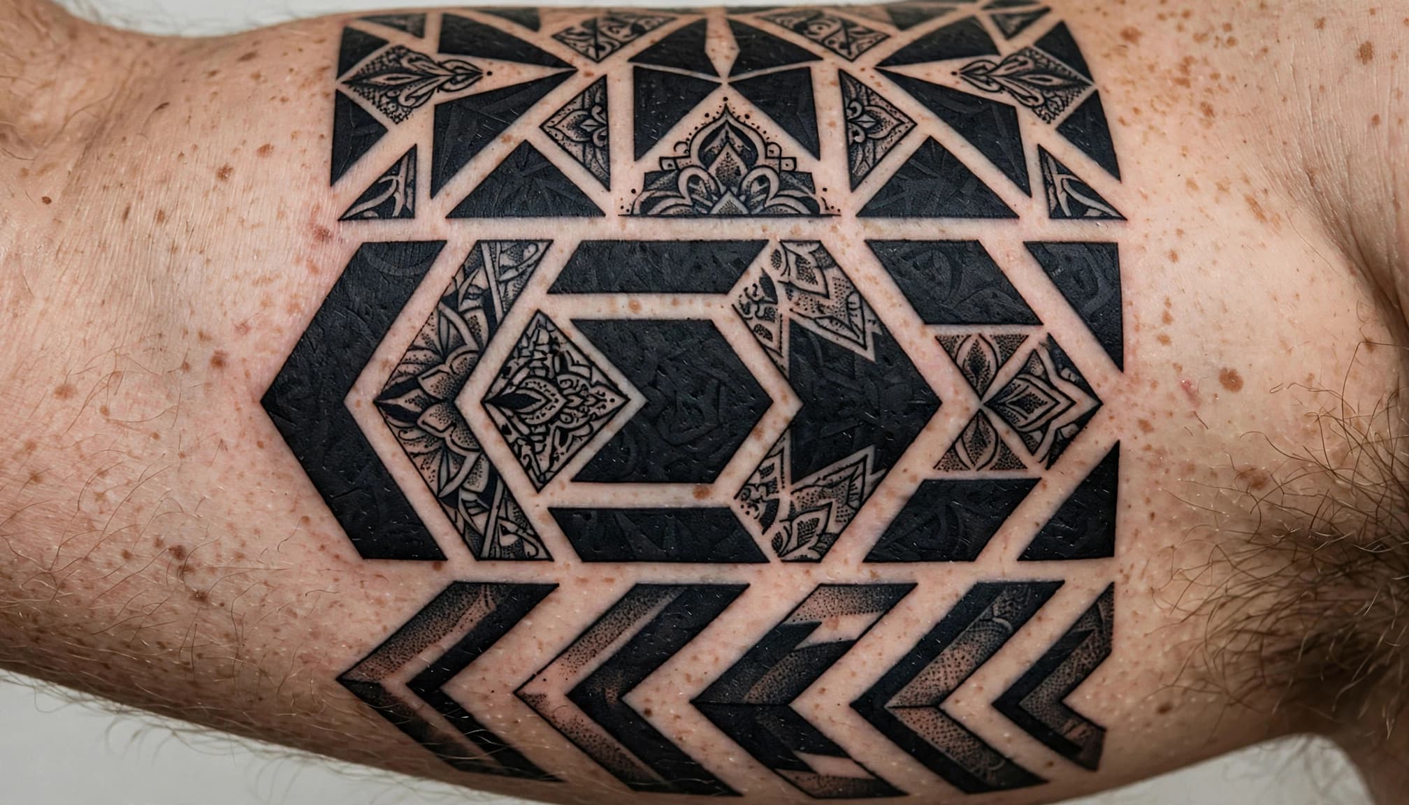A man's upper arm with a black geometric tattoo and exposed skin breaks.