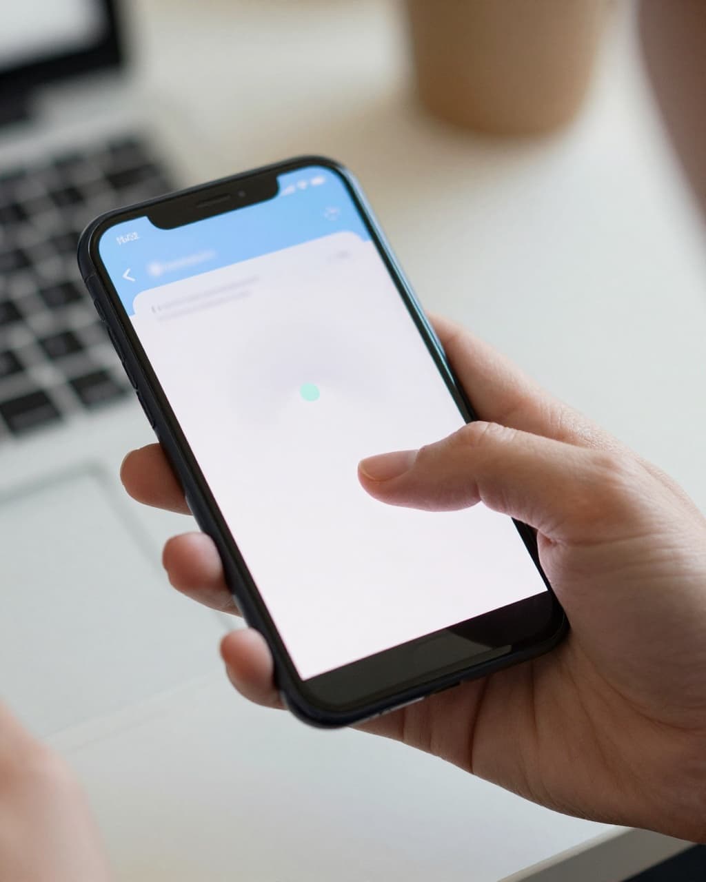 Close-up of a hand holding a smartphone with a blurred breathing app screen, person exhaling calmly in foreground, office desk background with natural light.