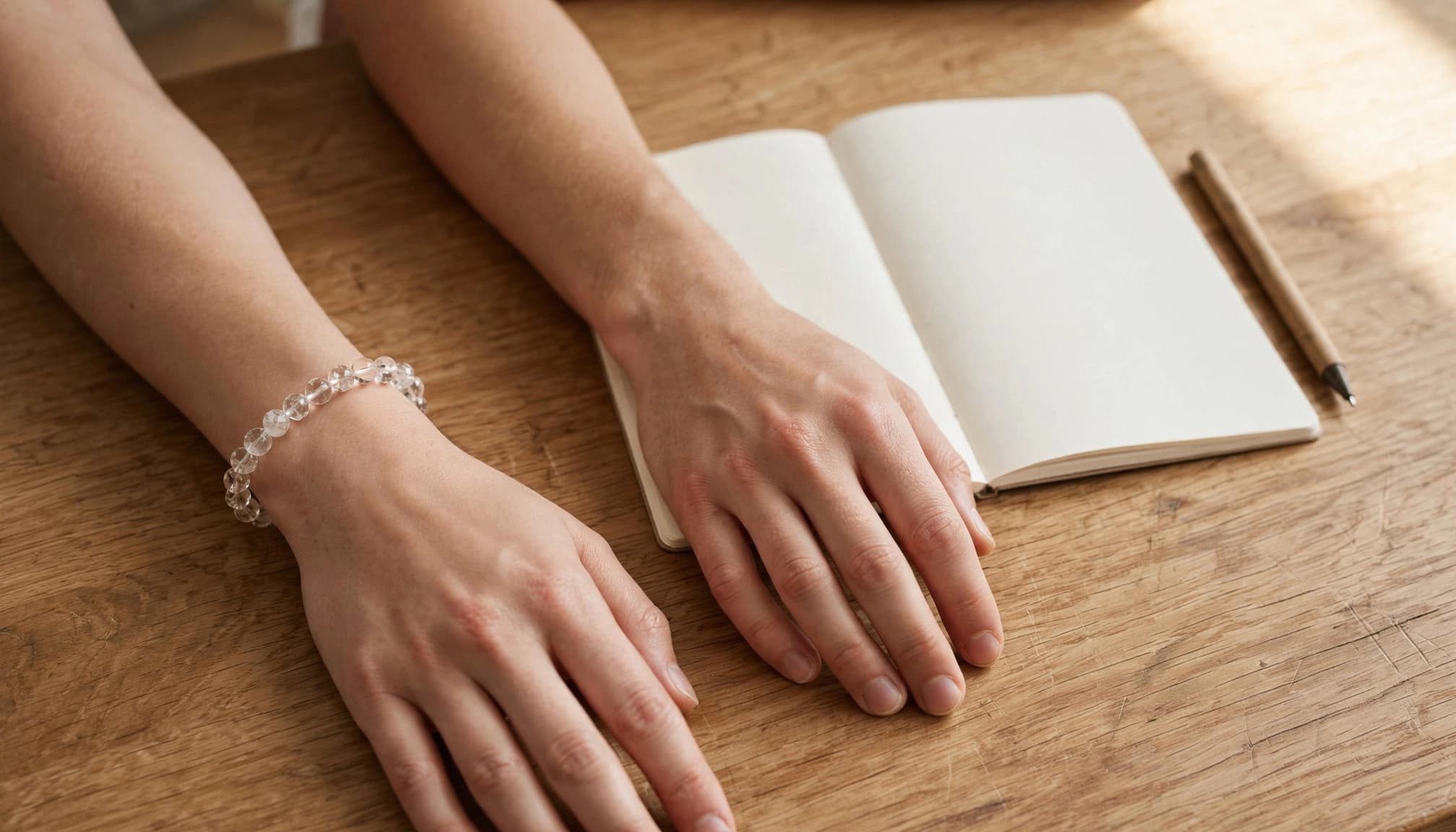 A crystal bracelet on one wrist beside an open notebook and pen.