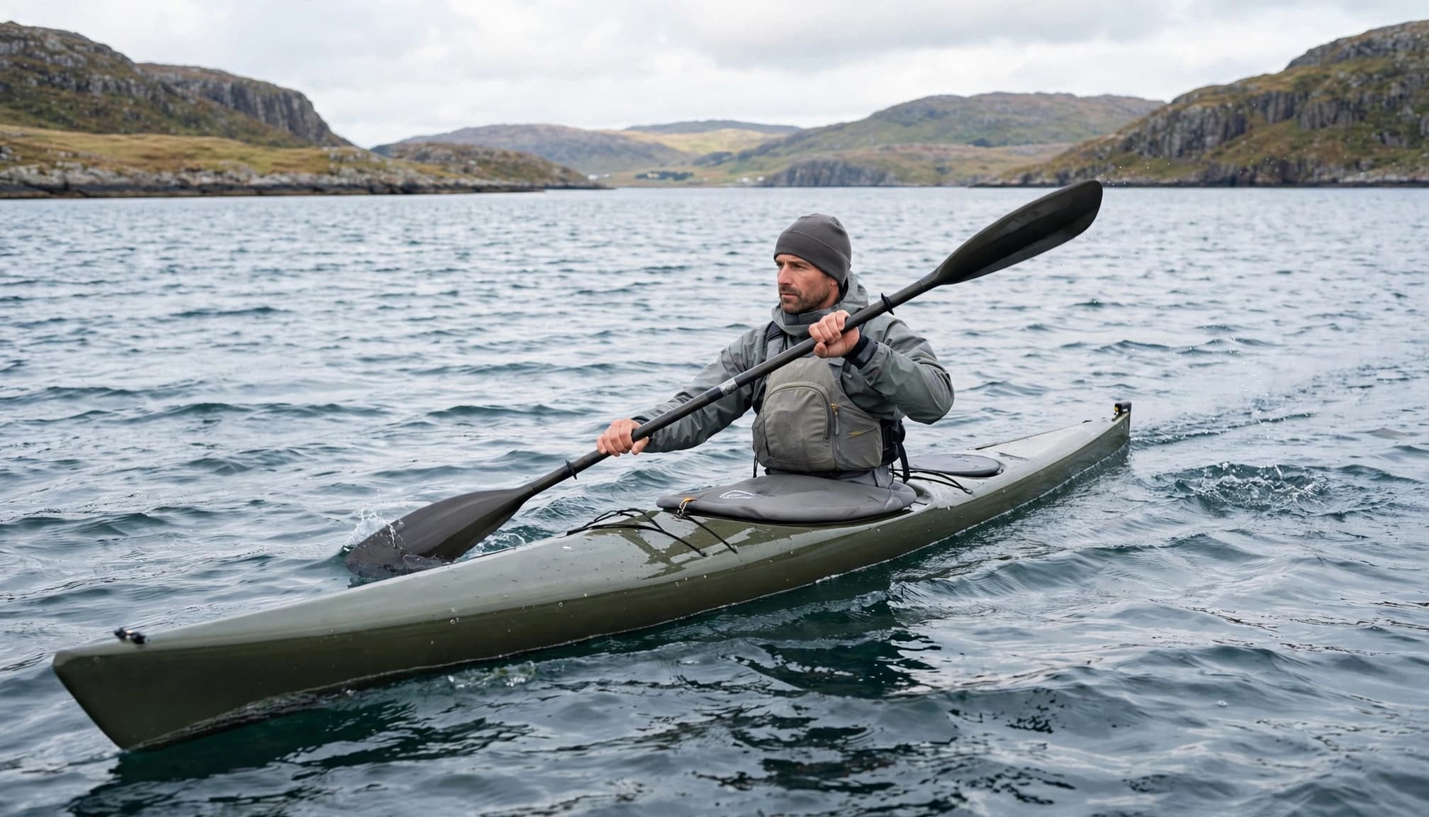 En kajakroer justerer pagajvinklen i sidevind på en åben fjord.