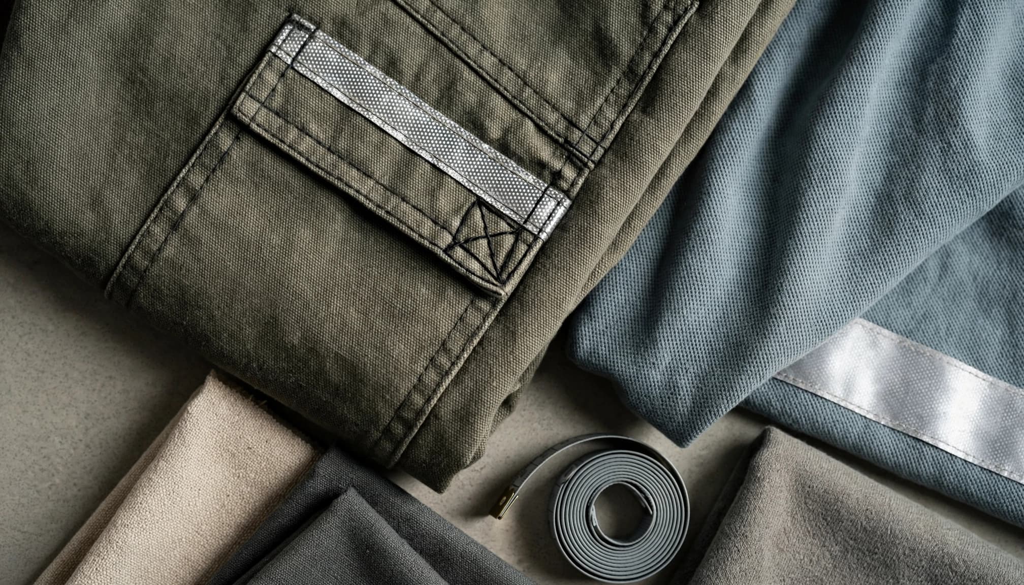 Workwear fabric, trouser seams, pockets, and reflective trim arranged with a tape measure and swatches.