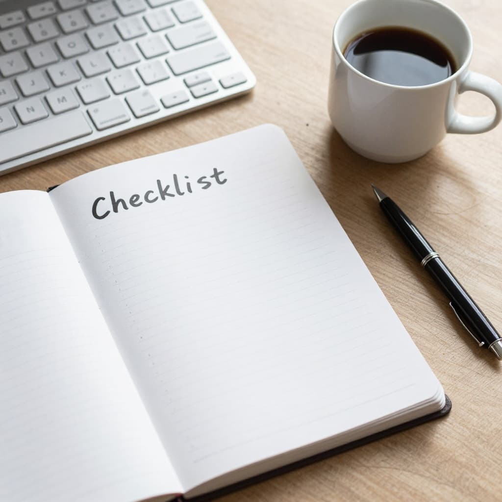 Top-down view of a notepad checklist next to a keyboard and coffee mug in a practical workspace, soft natural light, photorealistic square composition.
