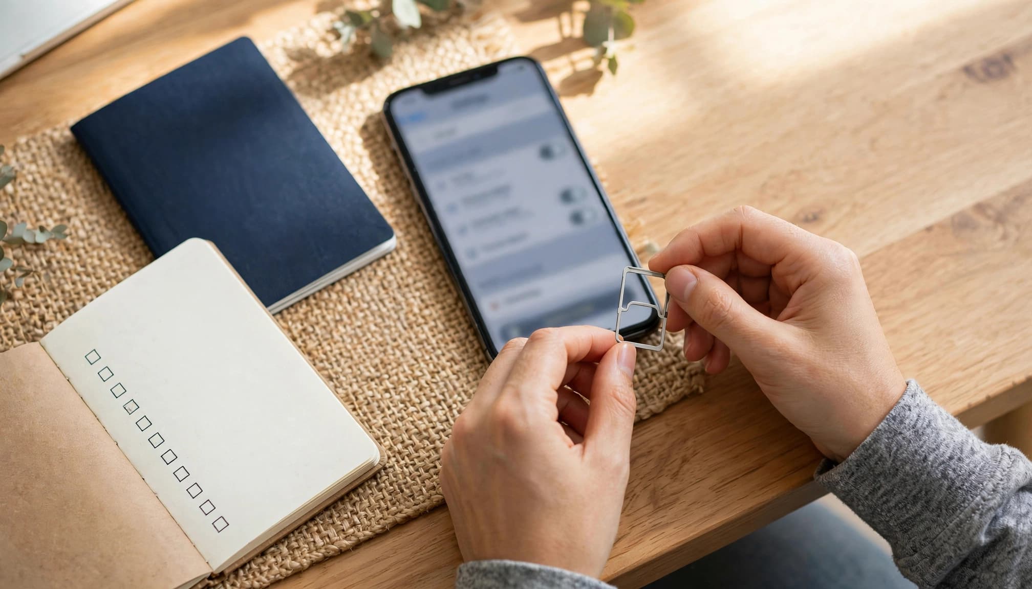 Hands organize a passport, phone, SIM tool, and notebook on an entryway table.