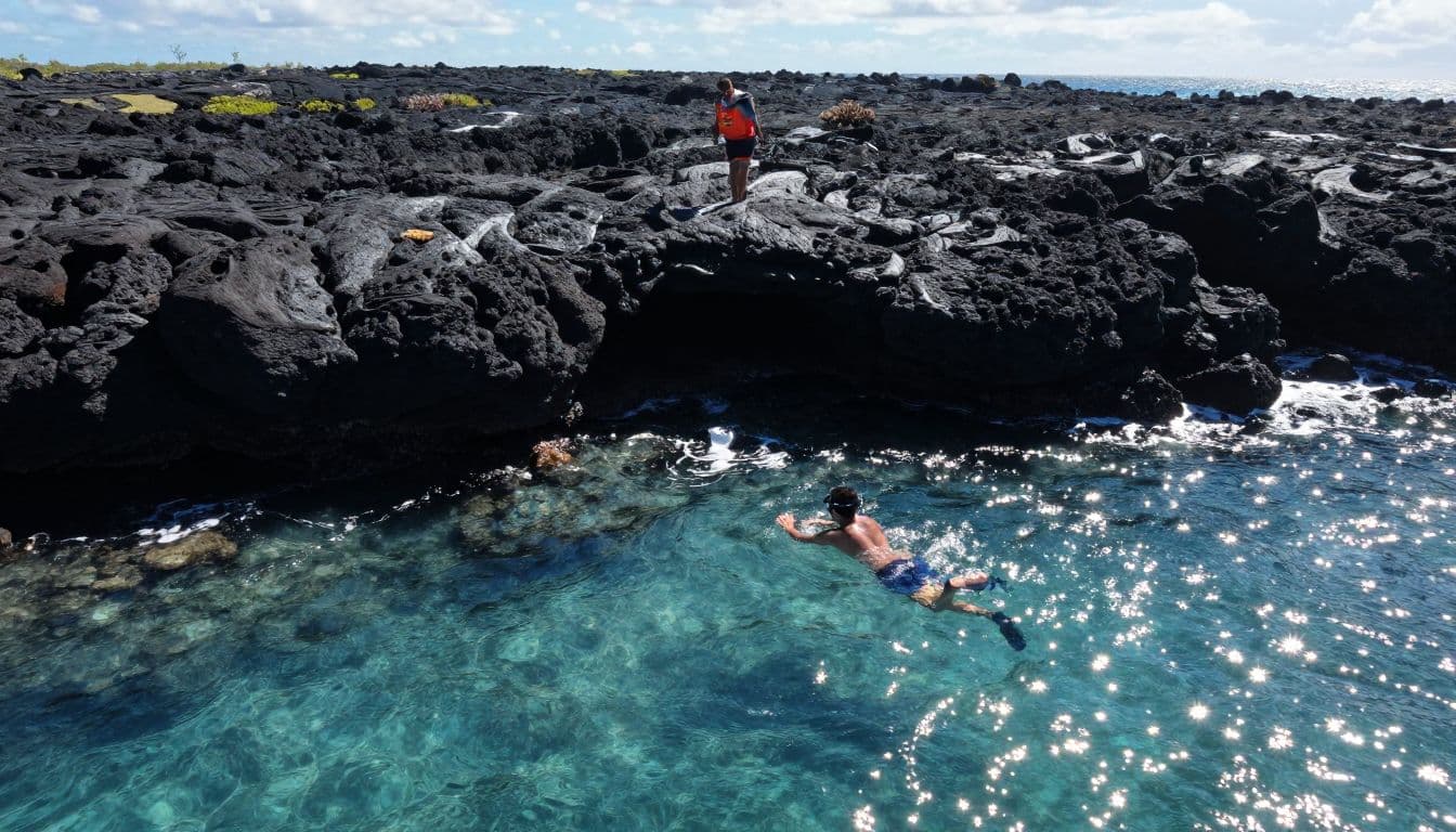 A snorkeler and guide view a lava reef and coral wall in clear Hawaiian water.