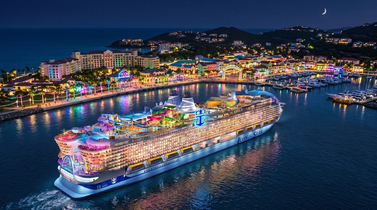 Aerial view of the Legend of the Seas cruise ship featuring multiple decks, colorful water slides, pools with palm trees, and the distinctive blue and white hull sailing on deep blue ocean waters.